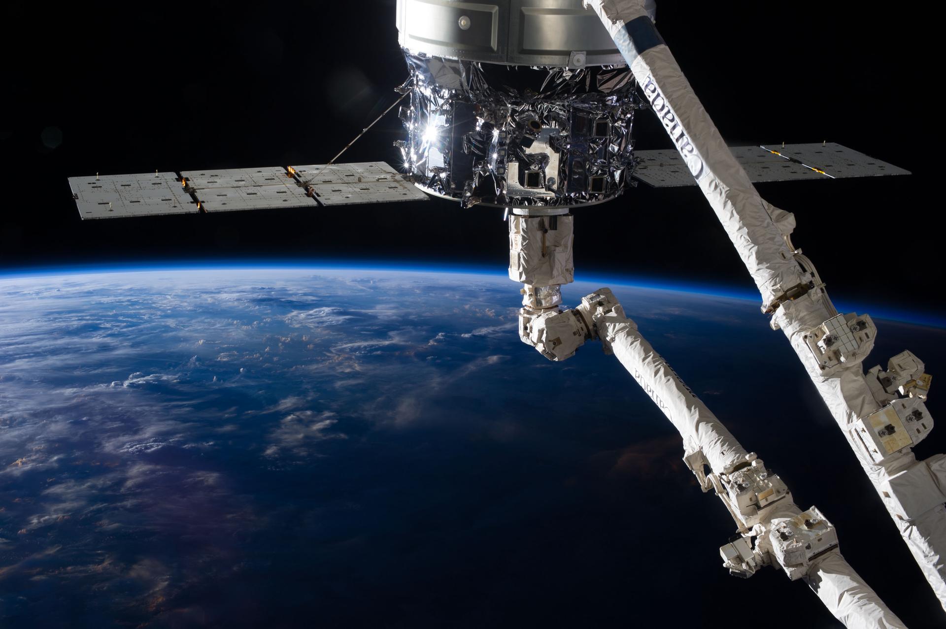 Canadarm2 robotic arm reaching toward a cargo spacecraft above Earth